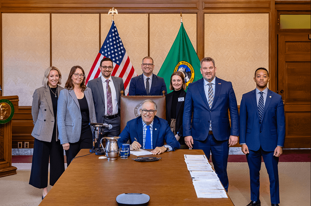 Group of professionals posing for a photo with an American and a state flag in the background, possibly in a governmental setting after a legislative update on passed animal bills.
