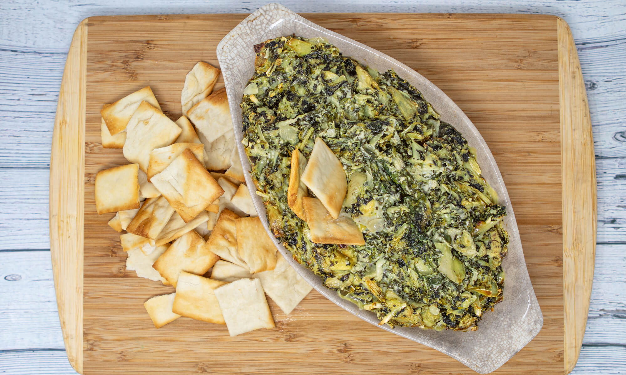 Oval dish of spinach artichoke dip on a wooden board, served with baked pita chips—perfect for your next Mocktail Party or as a tasty bite before a Seattle Cooking Class.