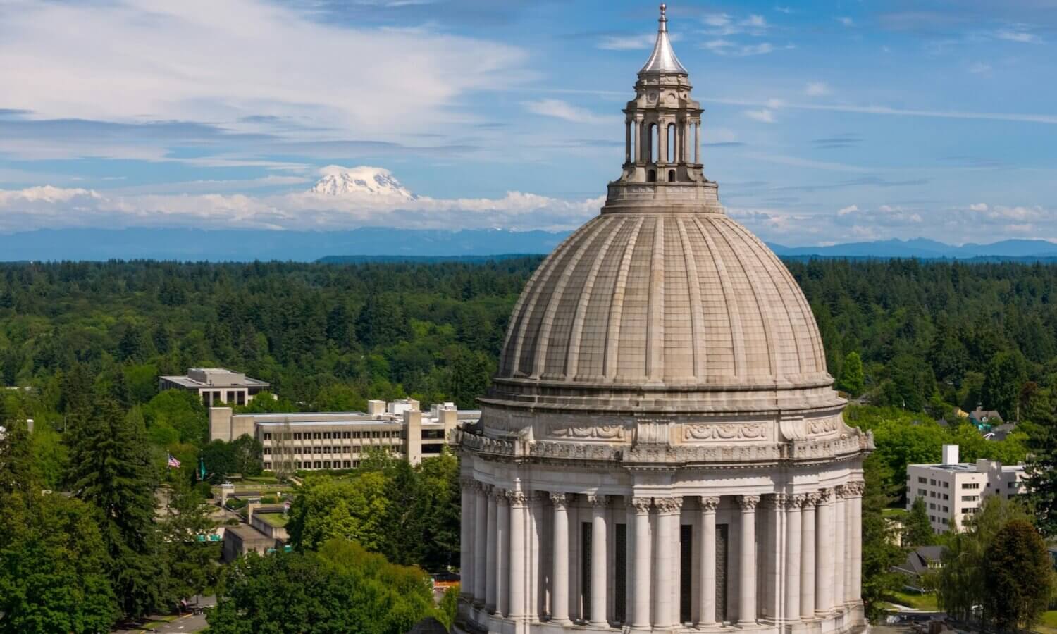 The Washington State Capitol dome in Olympia stands in the foreground, with Mount Rainier in the distance under a blue sky—a striking view as the 2026 Legislative Session approaches.