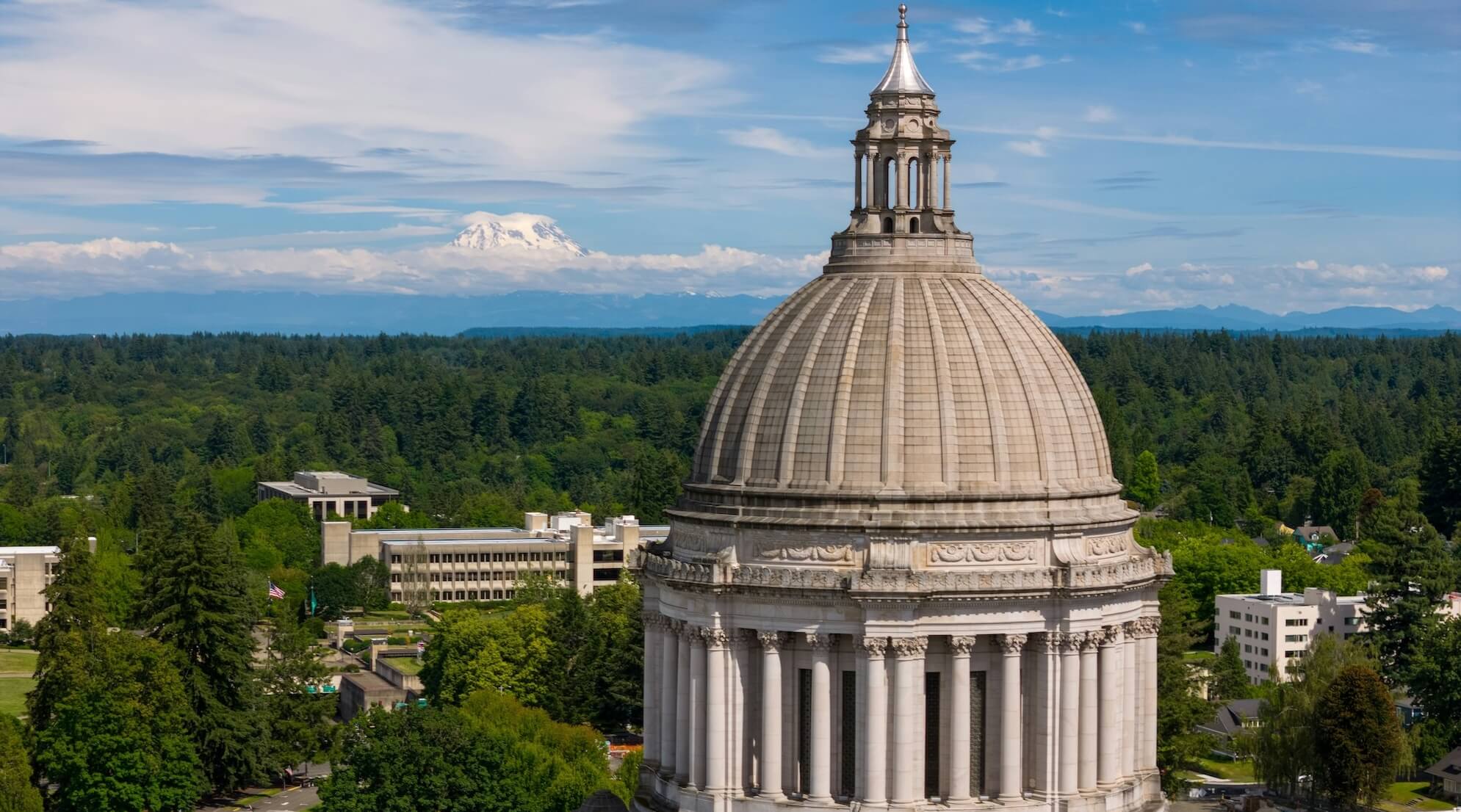 The Washington State Capitol dome in Olympia stands in the foreground, with Mount Rainier in the distance under a blue sky—a striking view as the 2026 Legislative Session approaches.