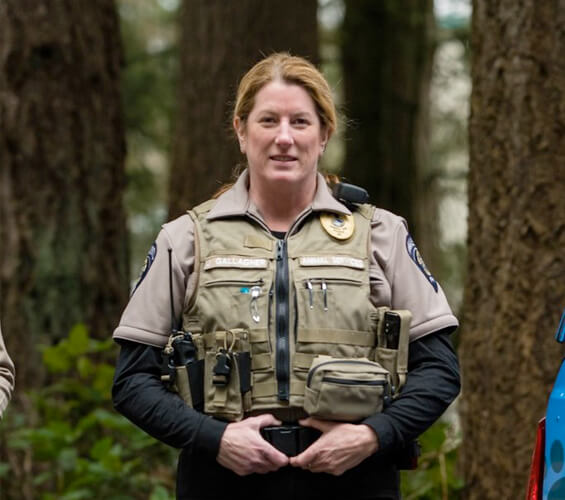 A uniformed officer, recipient of the Bucky Award for Excellence, stands outdoors in front of trees, facing the camera with hands clasped at her belt.